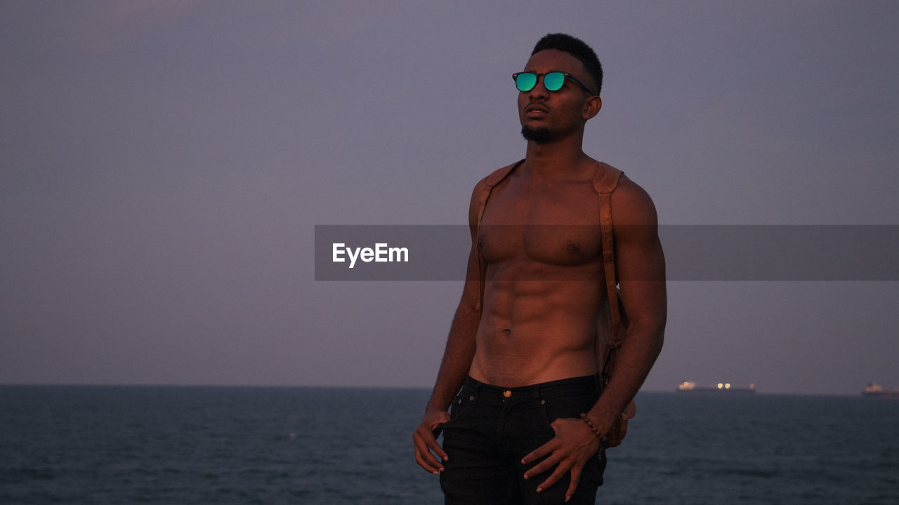 Shirtless man standing at beach against sky