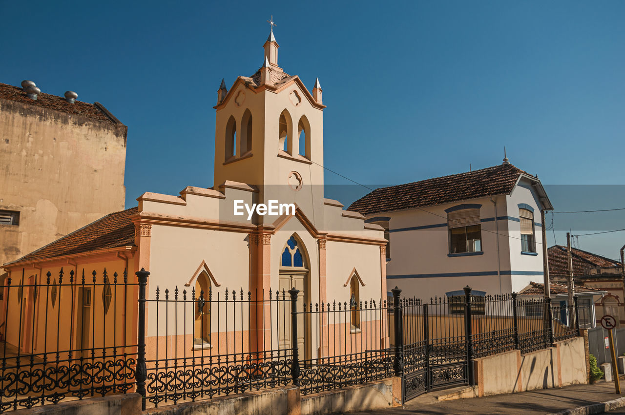 Facade of small church and belfry behind iron fence, in a sunny day at são manuel, brazil.