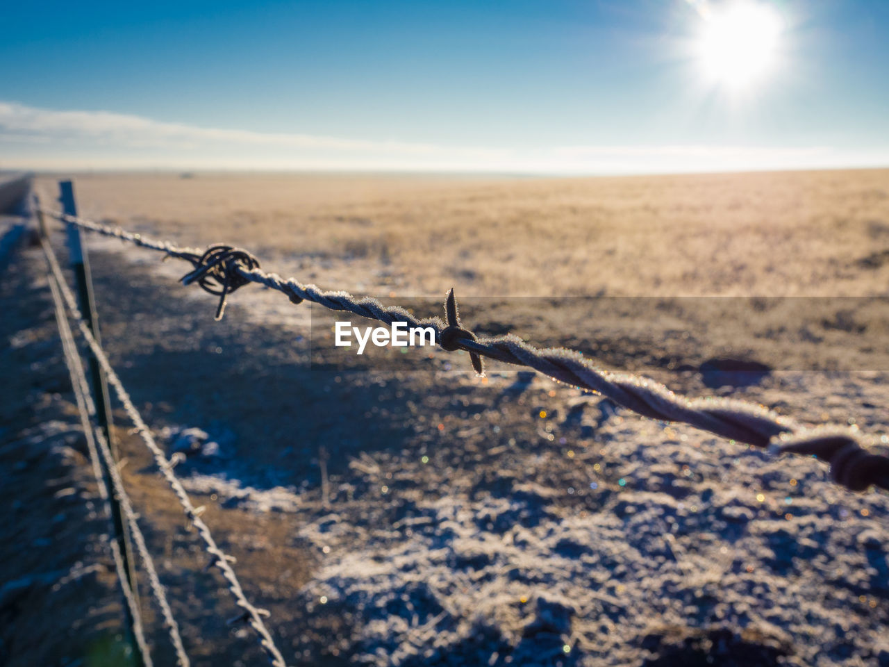 Close-up of frosted barbed wire fence on field against sky