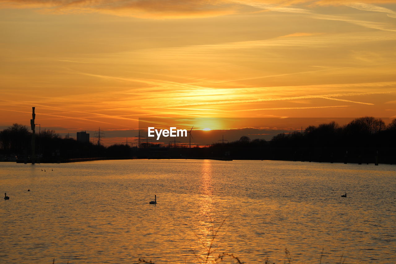 SILHOUETTE BIRDS BY LAKE AGAINST ORANGE SKY