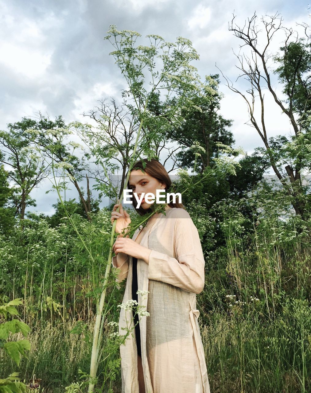 Portrait of woman standing by plant against sky