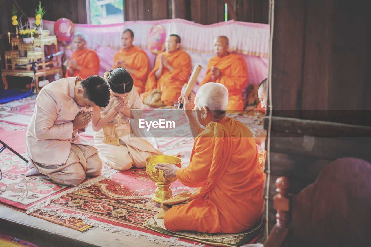 REAR VIEW OF PEOPLE SITTING AT TEMPLE