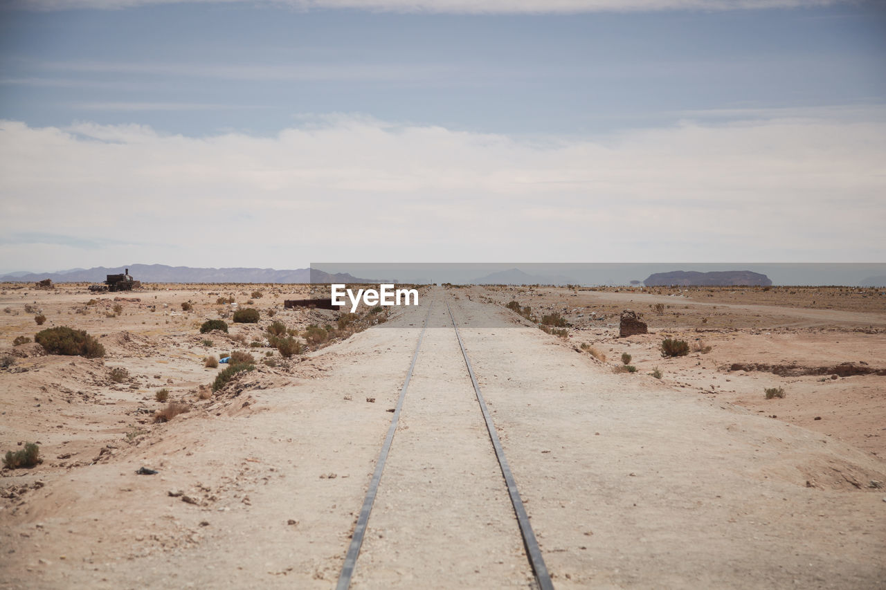Railroad track in desert against cloudy sky
