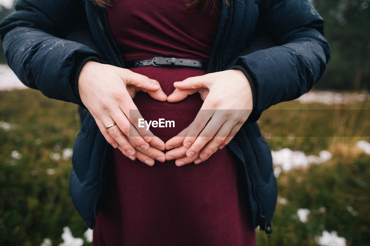 Midsection of couple making heart shape on pregnant belly