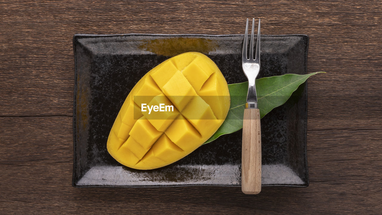 Tasty fresh yellow ripe mango with fork and mango leaf in rectangular ceramic plate on rustic wood