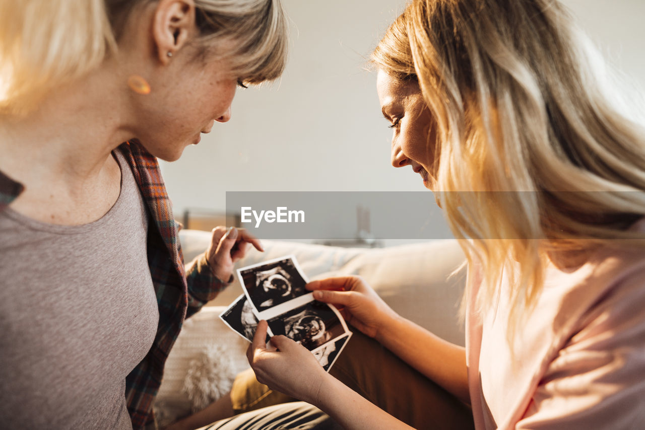 Woman discussing over ultrasound with pregnant sister at home