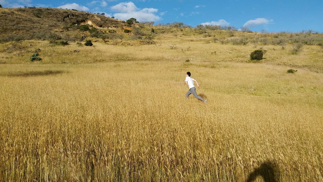 Man running on grassy field against sky