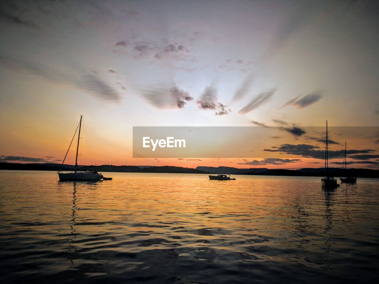 Silhouette boats sailing in sea against dramatic sky during sunset