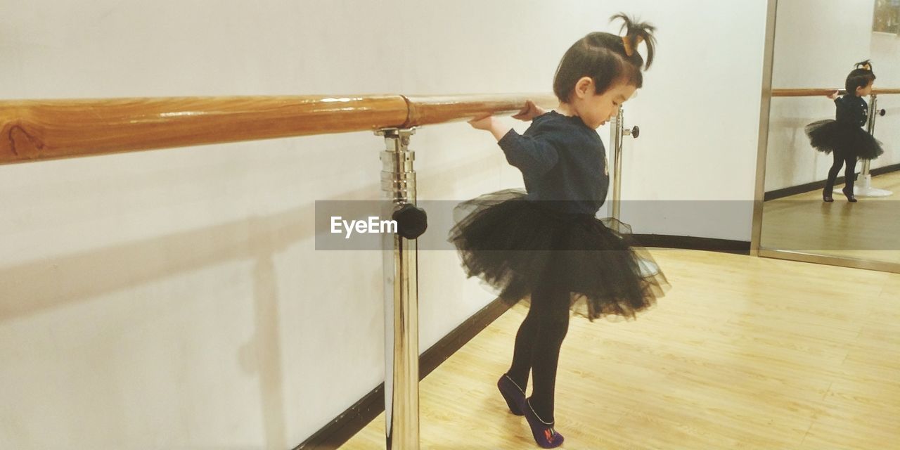 Side view of girl in tutu practicing tiptoe on hardwood floor