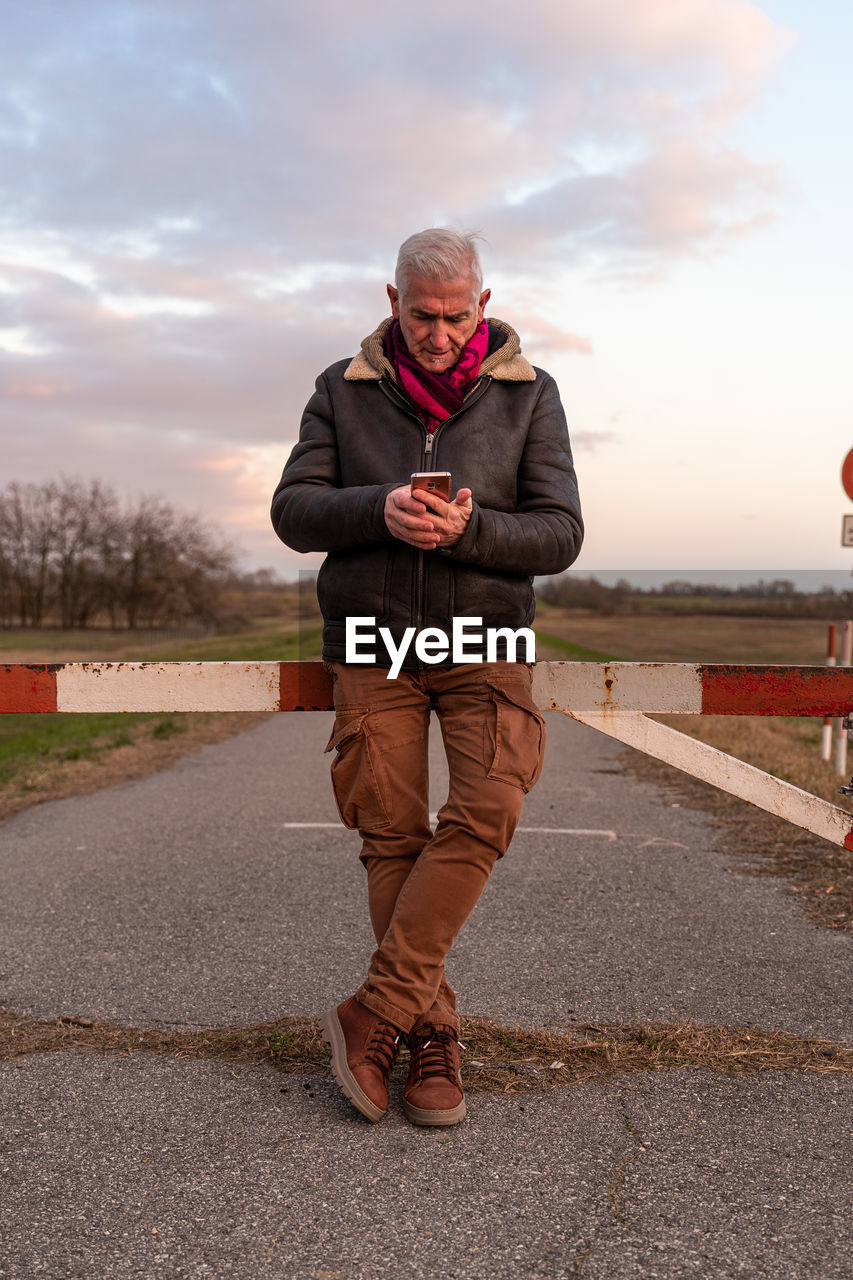 one person, adult, cloud, sky, full length, men, standing, senior adult, footwear, person, nature, clothing, front view, road, seniors, lifestyles, red, sports, day, mature adult, outdoors, spring, city, transportation, technology