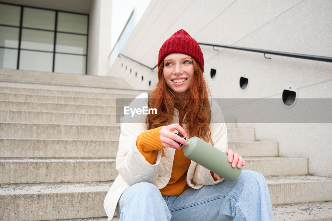 portrait of young woman using mobile phone while sitting on staircase