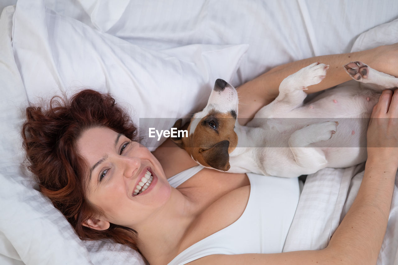 Happy woman with dog relaxing on bed at home