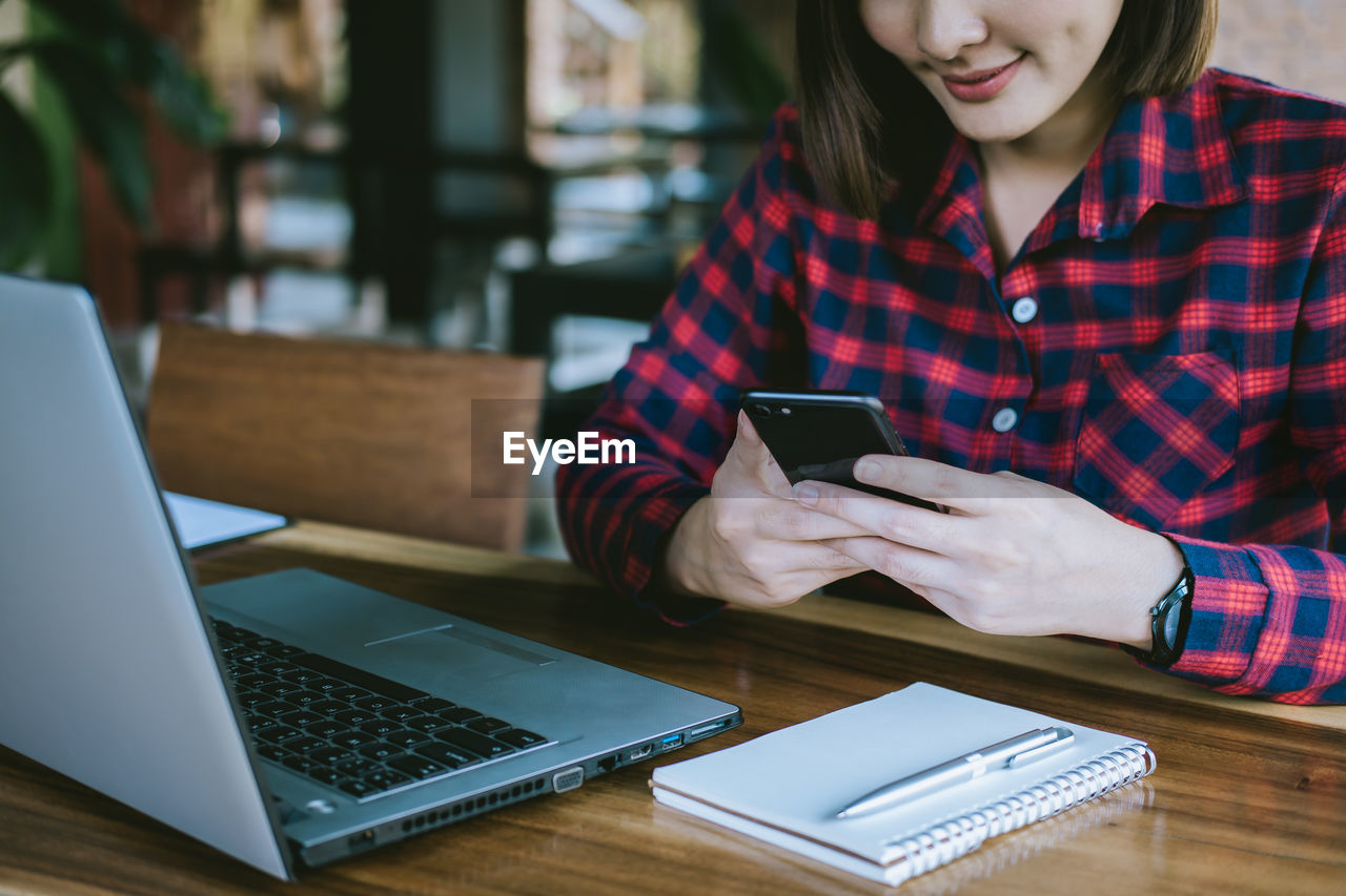 Midsection of woman using mobile phone while sitting at table