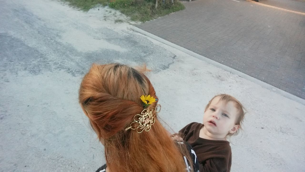 Rear view of mother wearing flower carrying toddler on street