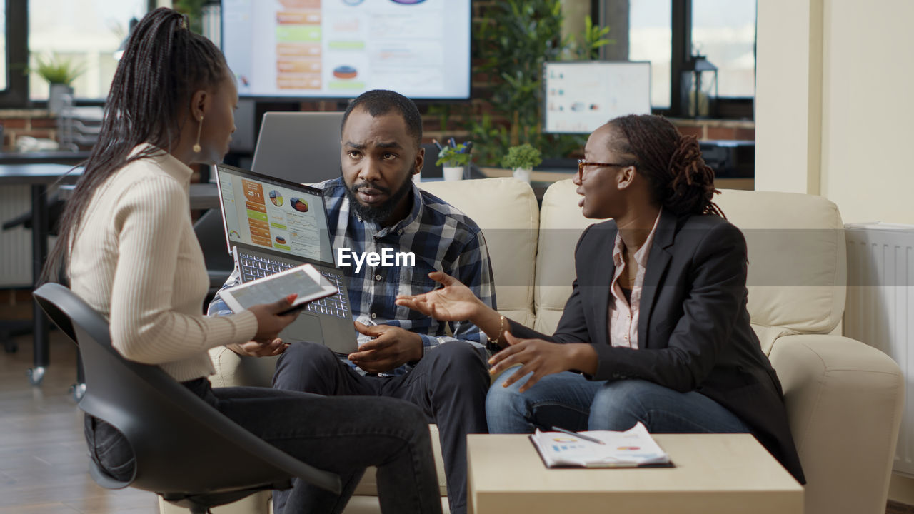 Businessman showing laptop to colleague sitting by businesswoman in office