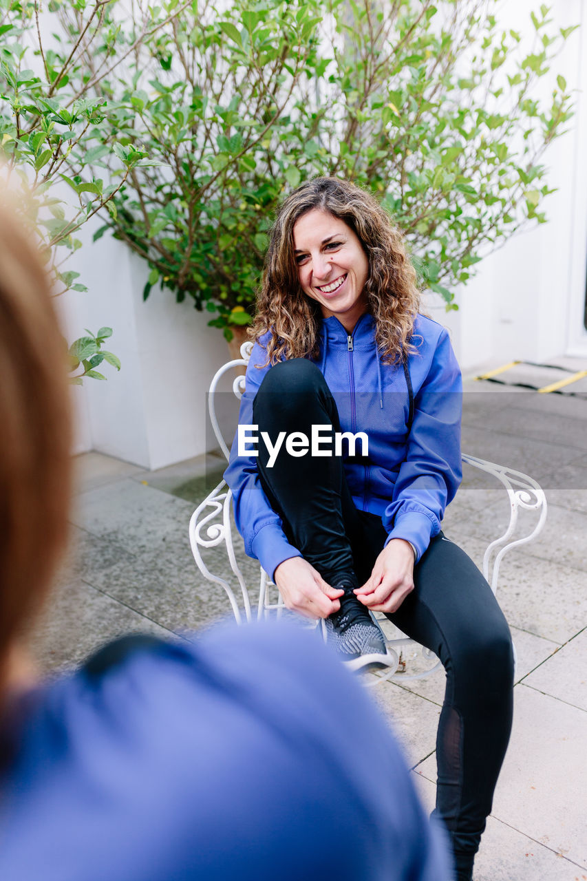 High angle view of smiling young woman tying sports shoe while sitting on chair