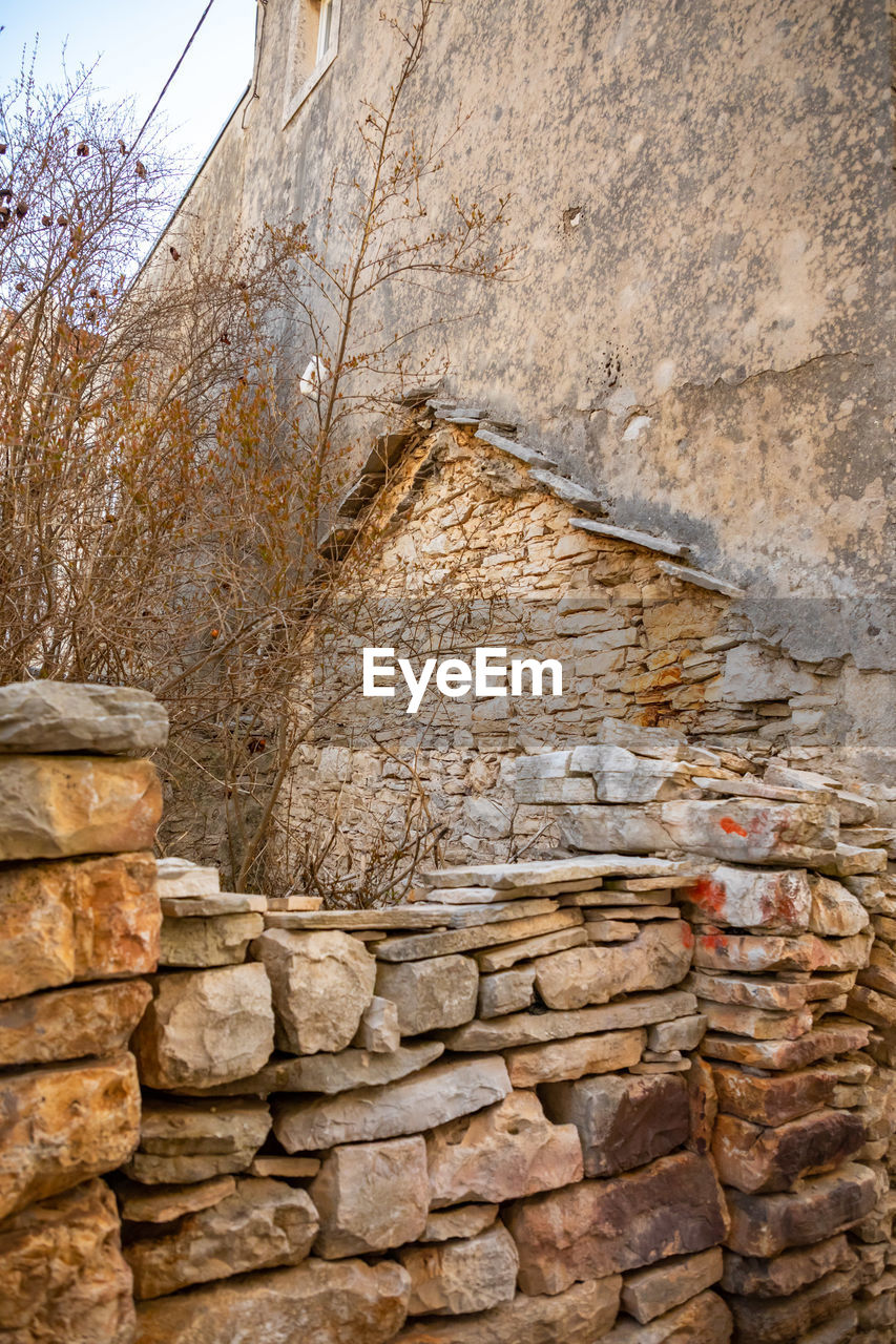 CLOSE-UP OF STONE WALL AGAINST BUILDING AND TREES