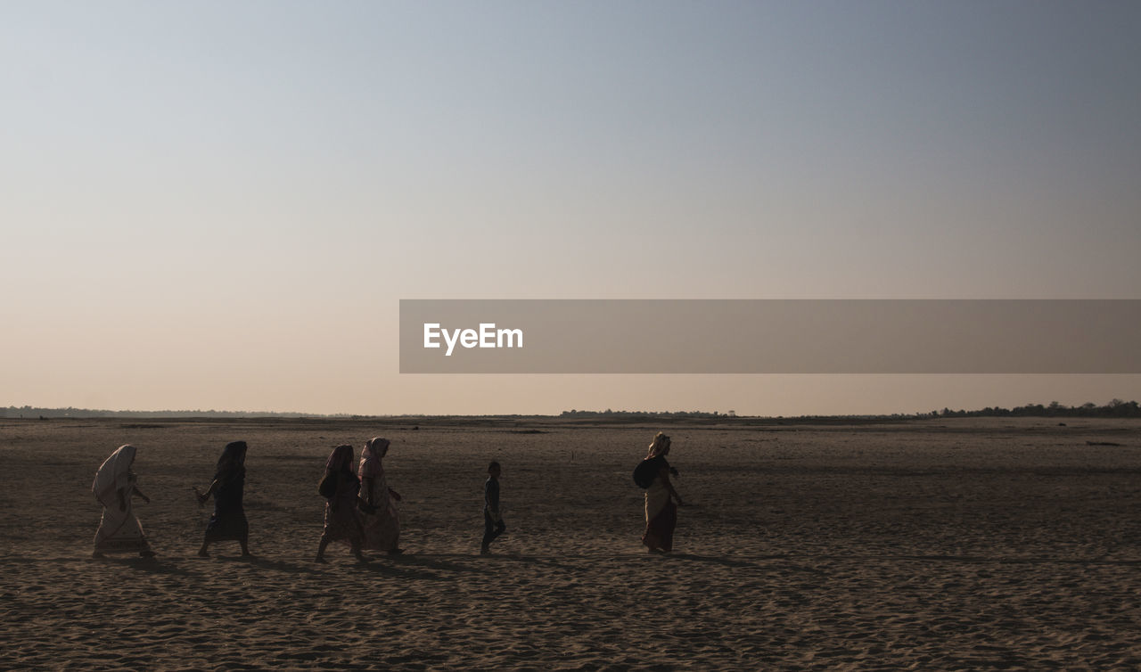 People on beach against clear sky during sunset