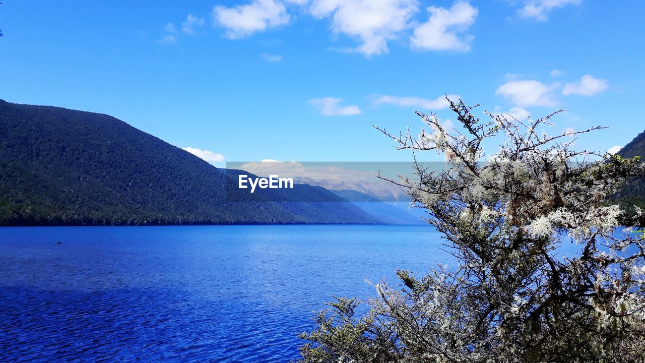 SCENIC VIEW OF SEA BY MOUNTAINS AGAINST BLUE SKY