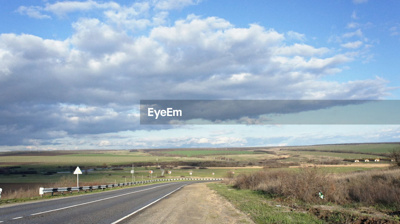 Road passing through landscape against cloudy sky