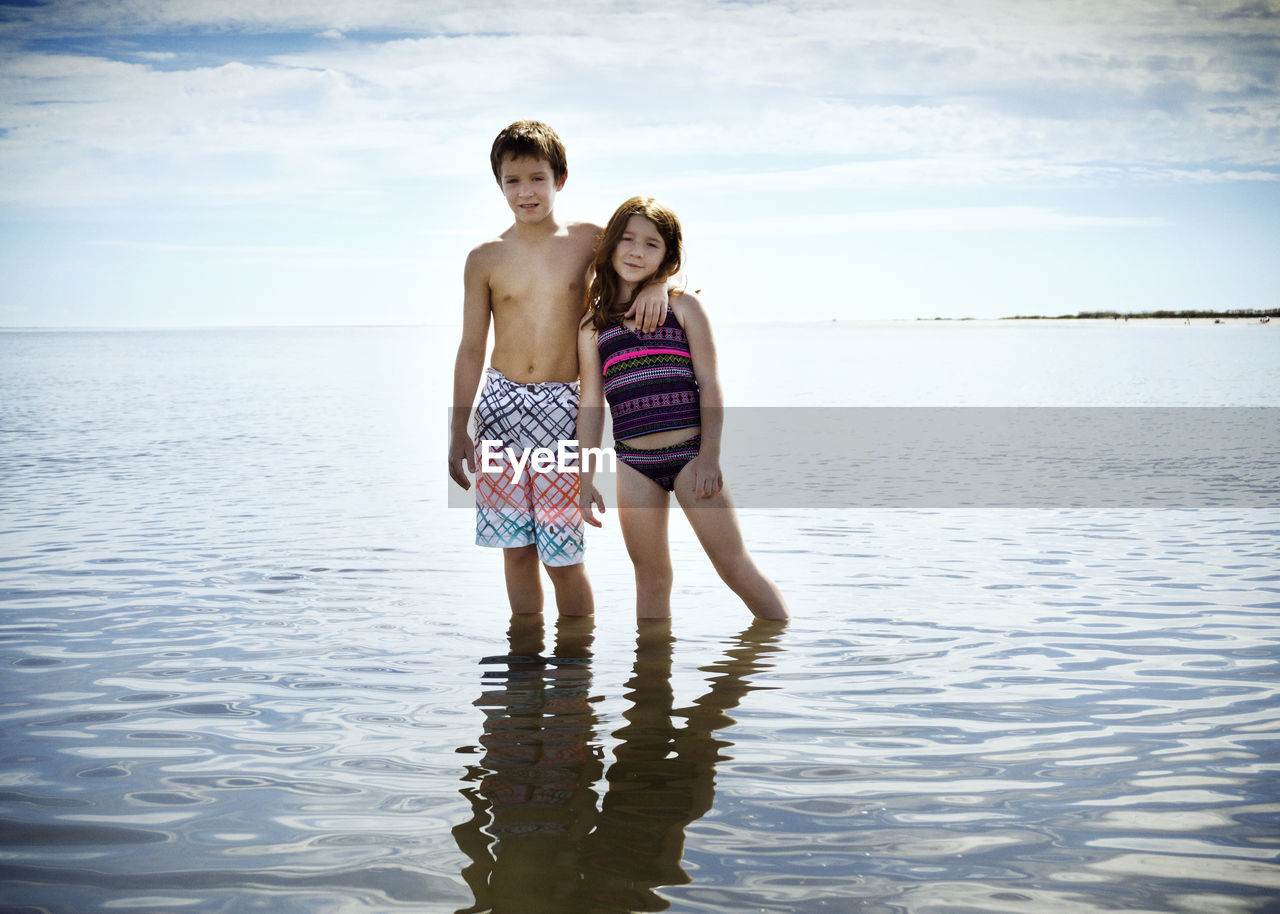 Portrait of brother standing with arm around sister on sea shore