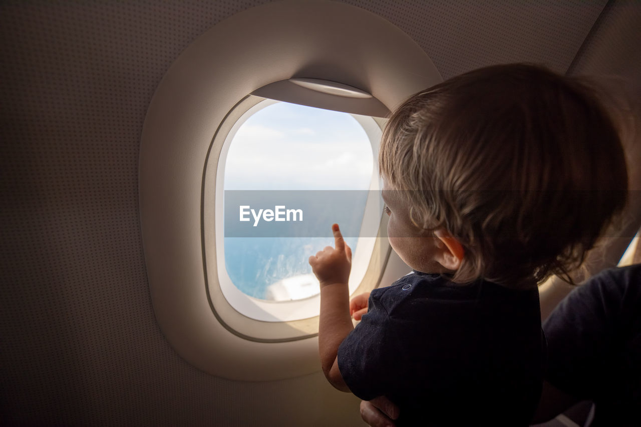 Rear view of boy looking through airplane window