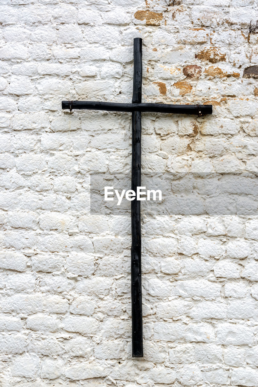 Black wooden cross on old white wall