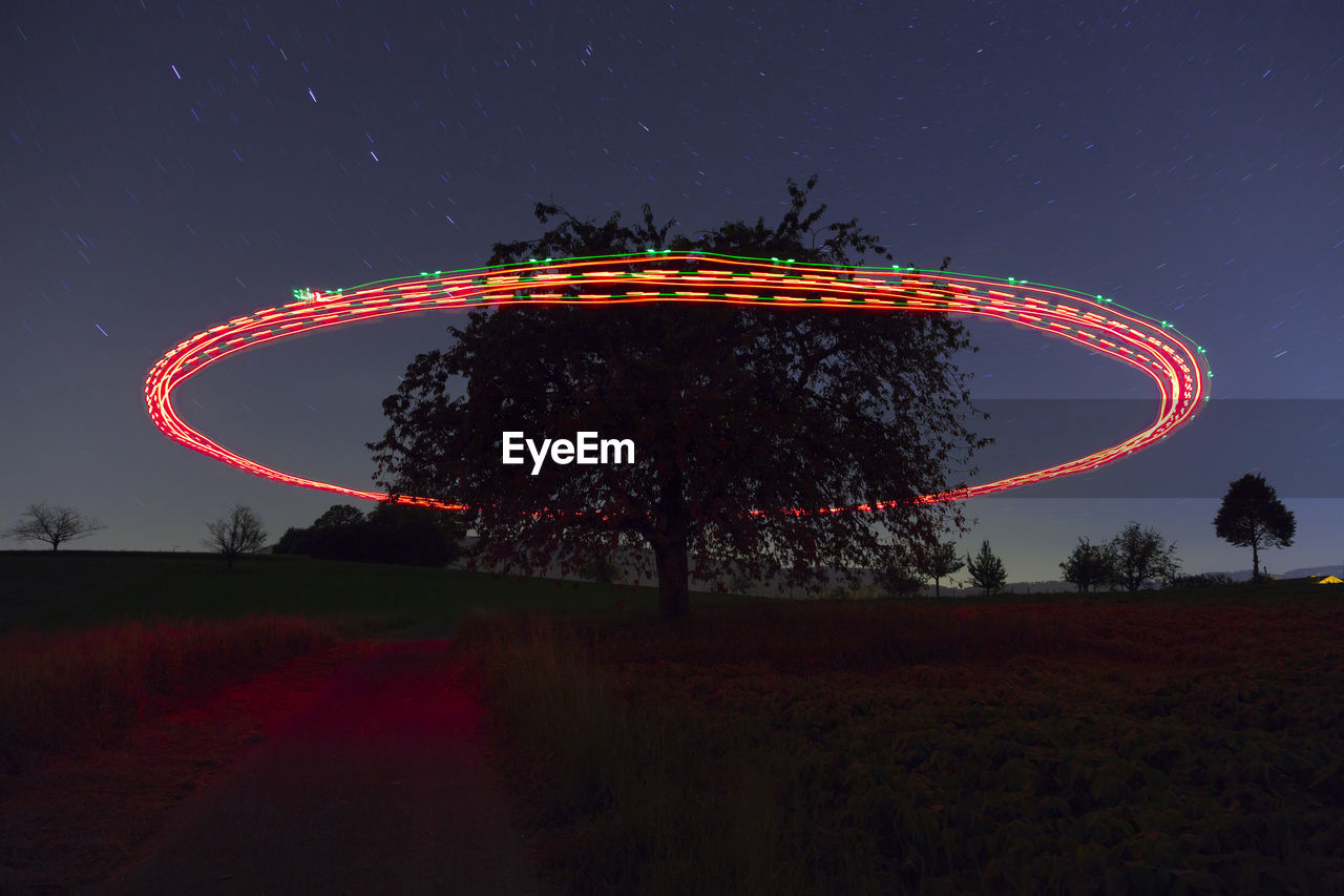 Low angle view of illuminated light painting by tree against sky at night