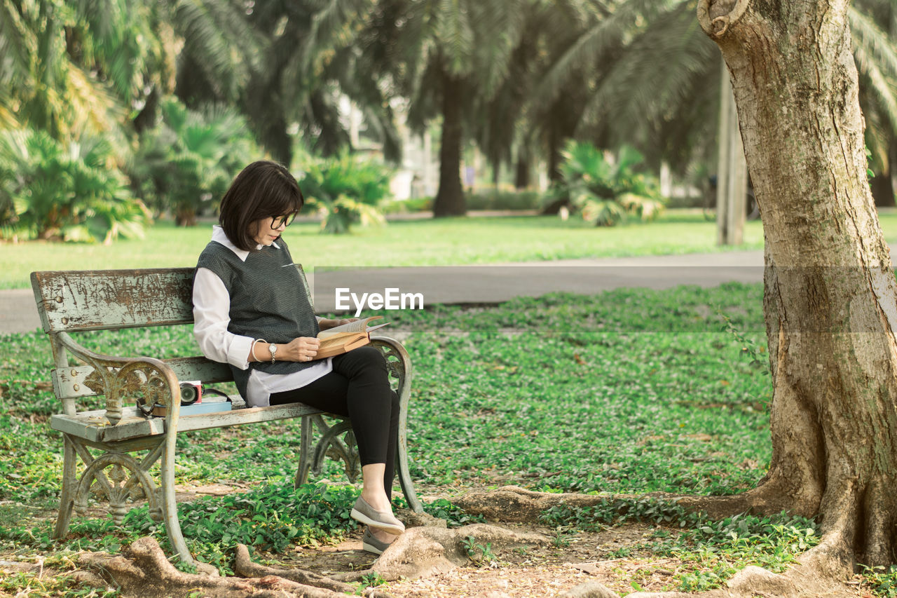 Woman reading book while sitting on bench at park