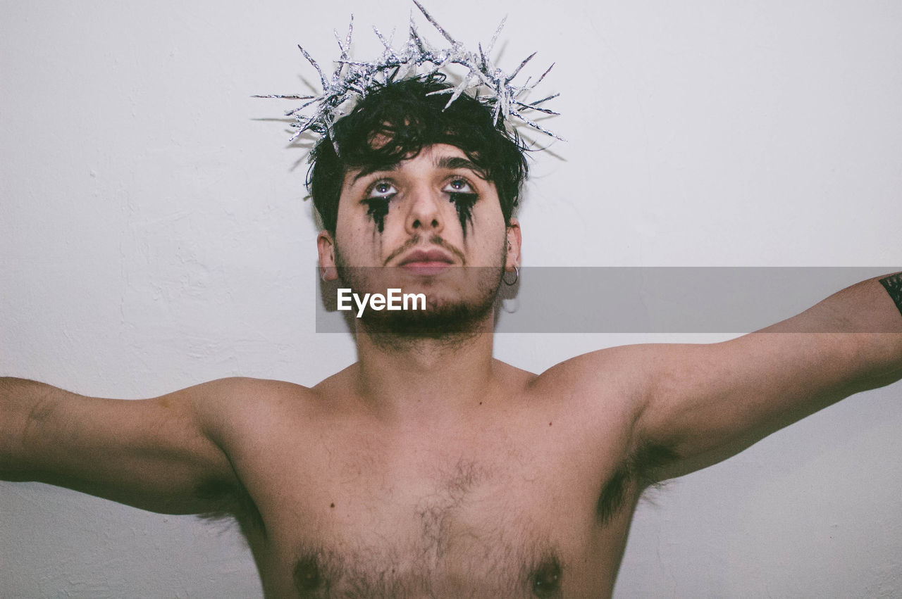 Close-up of shirtless man with make-up standing against wall