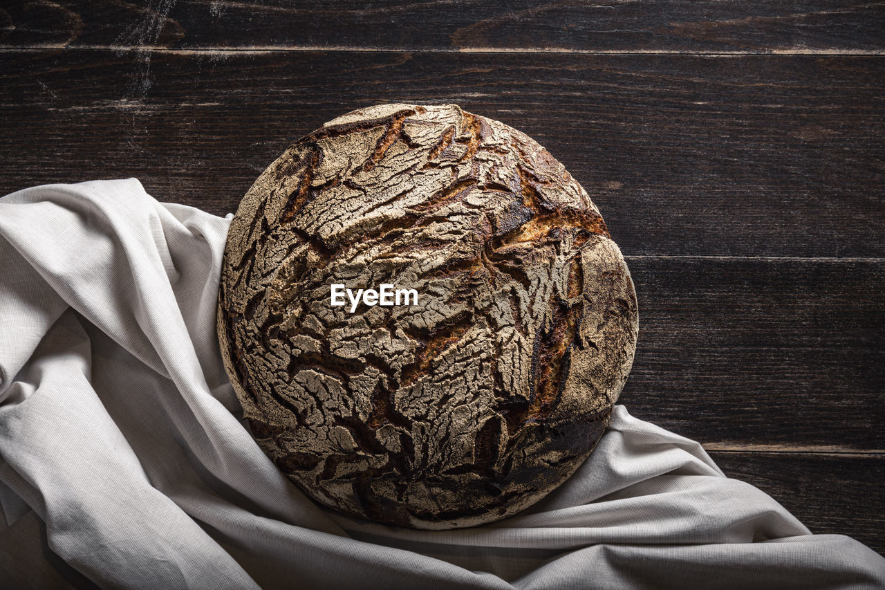 Bun of brown rye bread on table by cloth