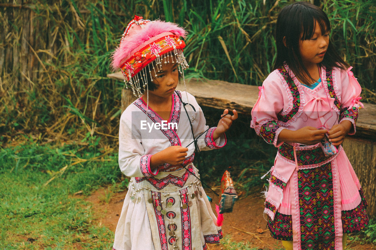 CUTE GIRL HOLDING UMBRELLA STANDING AGAINST TRADITIONAL CLOTHING