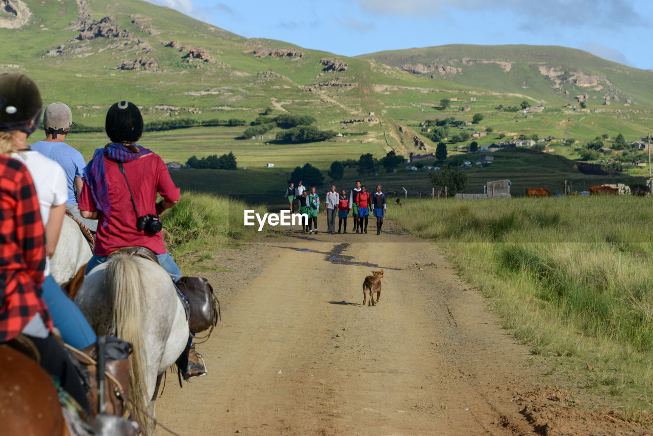 REAR VIEW OF PEOPLE RIDING ON FIELD