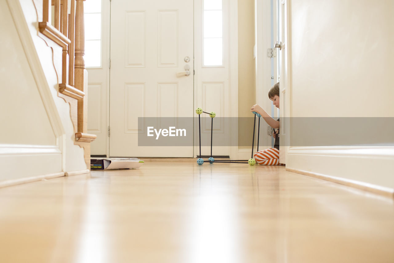 Young boy sits in sunny bright hallway playing with building toys