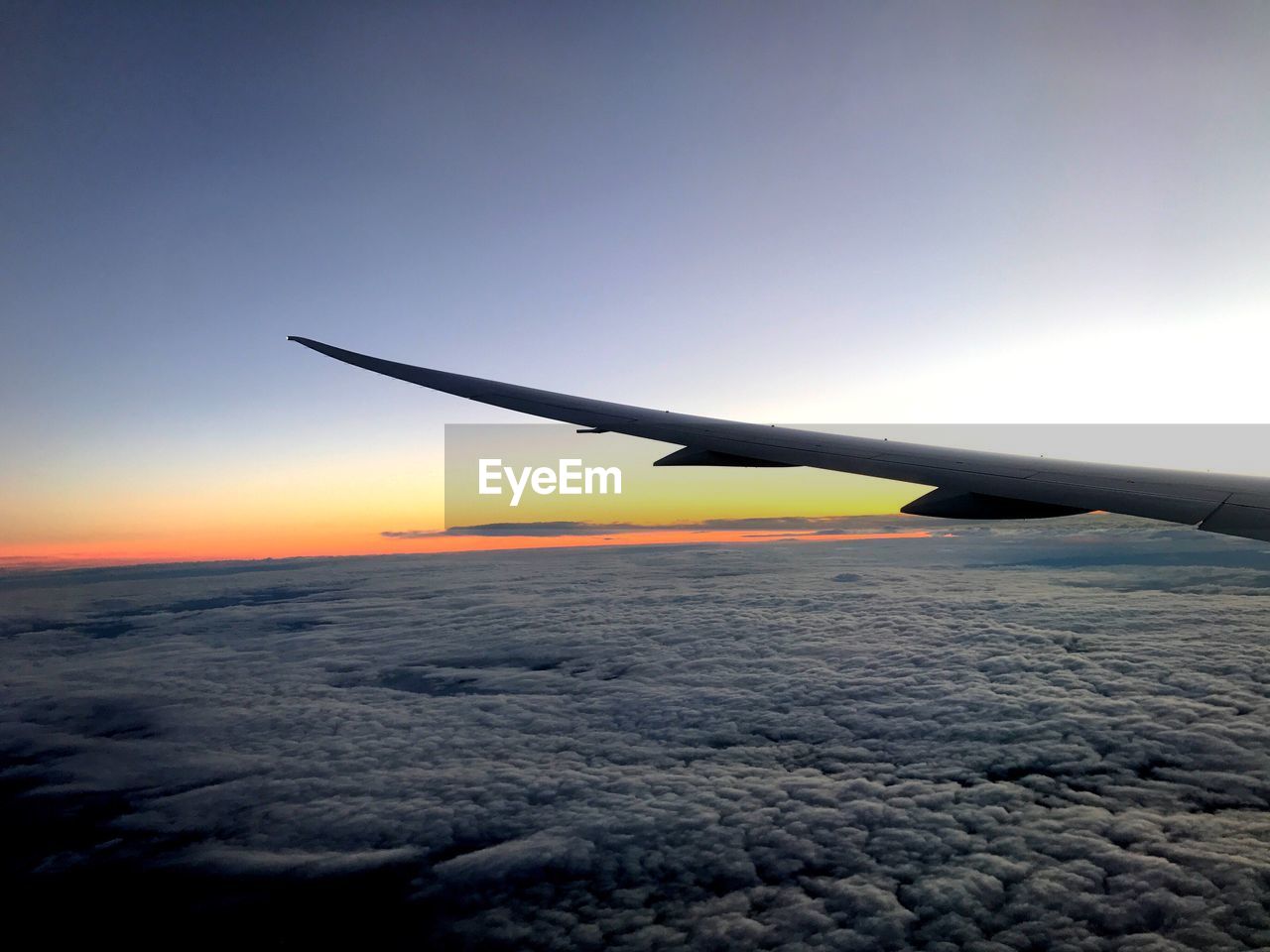 Cropped image of aircraft wing over cloudscape during sunset