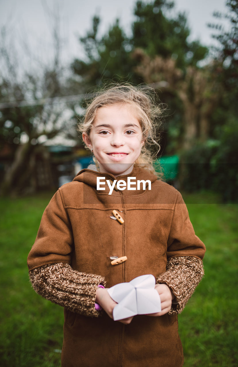 Portrait of smiling girl wearing jacket holding craft while standing in yard