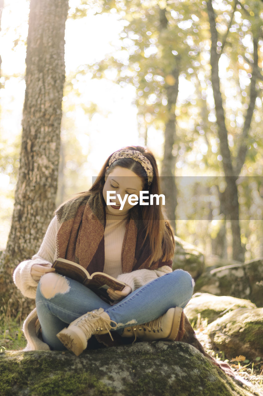 Young woman reading a book sitting and surrounded by a forest