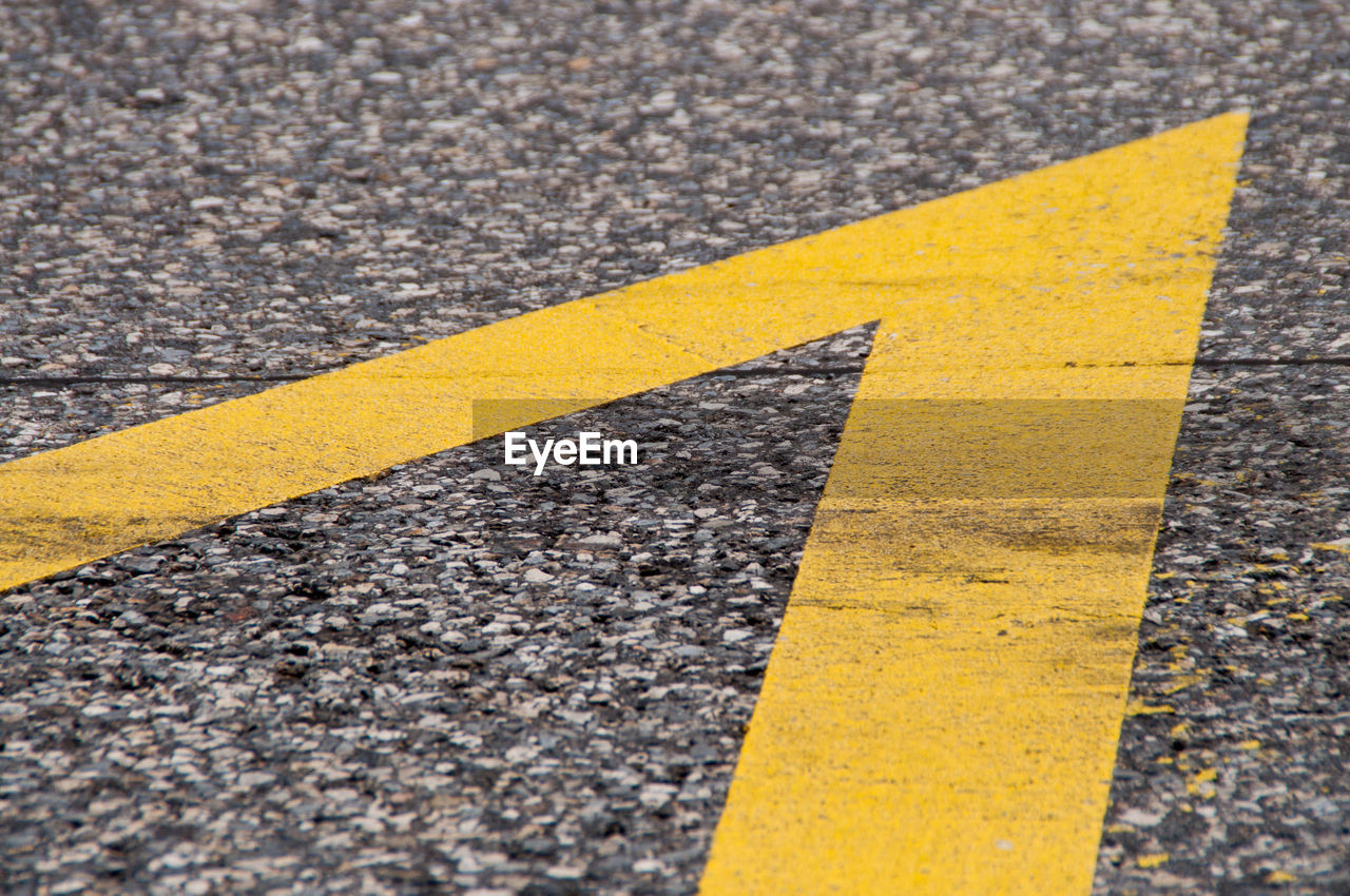 CLOSE-UP OF YELLOW ARROW SYMBOL ON ROAD