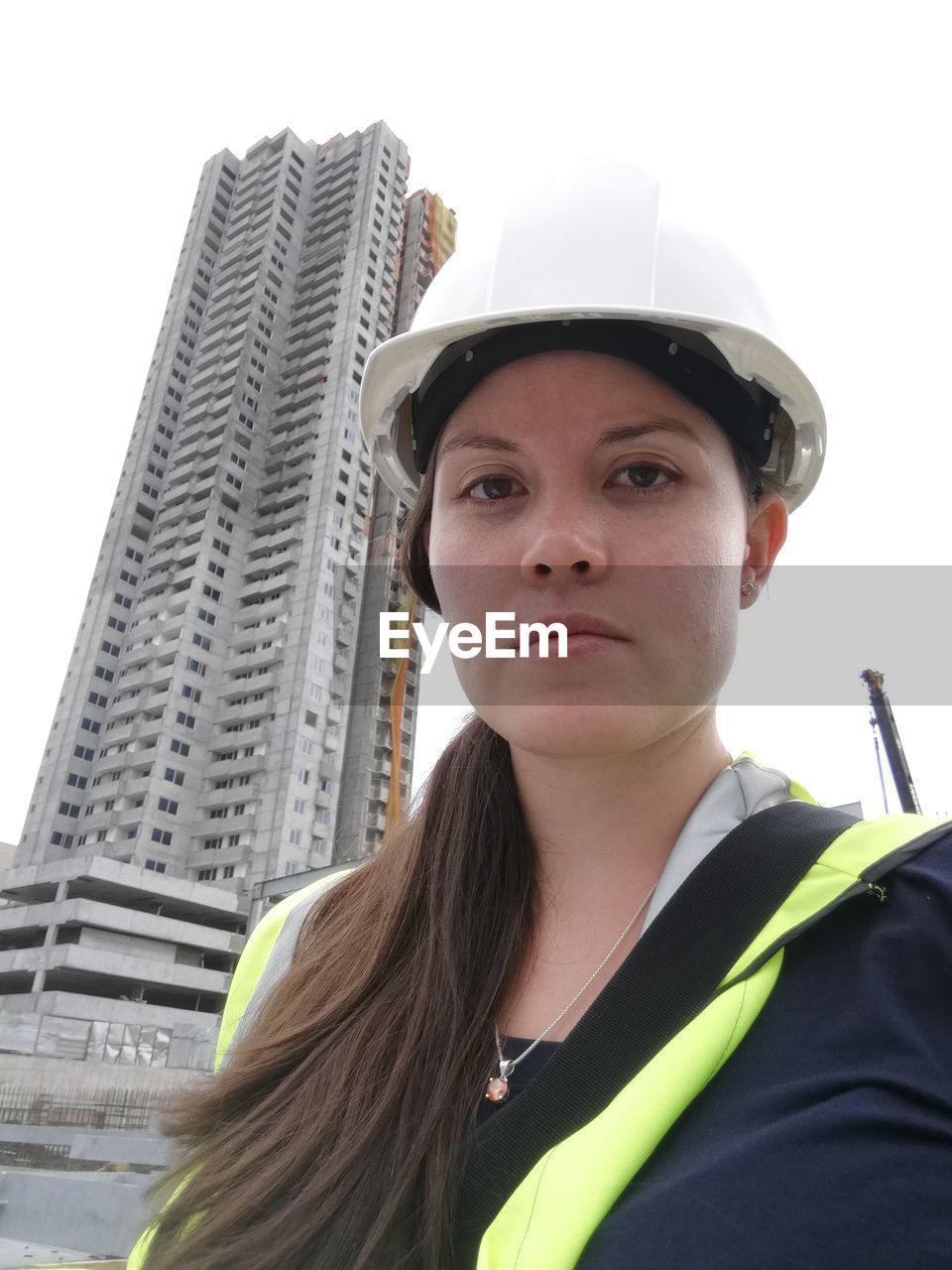 portrait, one person, adult, architecture, young adult, built structure, clothing, city, building exterior, headshot, looking at camera, women, person, occupation, hat, construction industry, serious, skyscraper, office building exterior, day, low angle view, headwear, business, protection, hard hat, building, standing, sky, outdoors, helmet, looking, industry, working