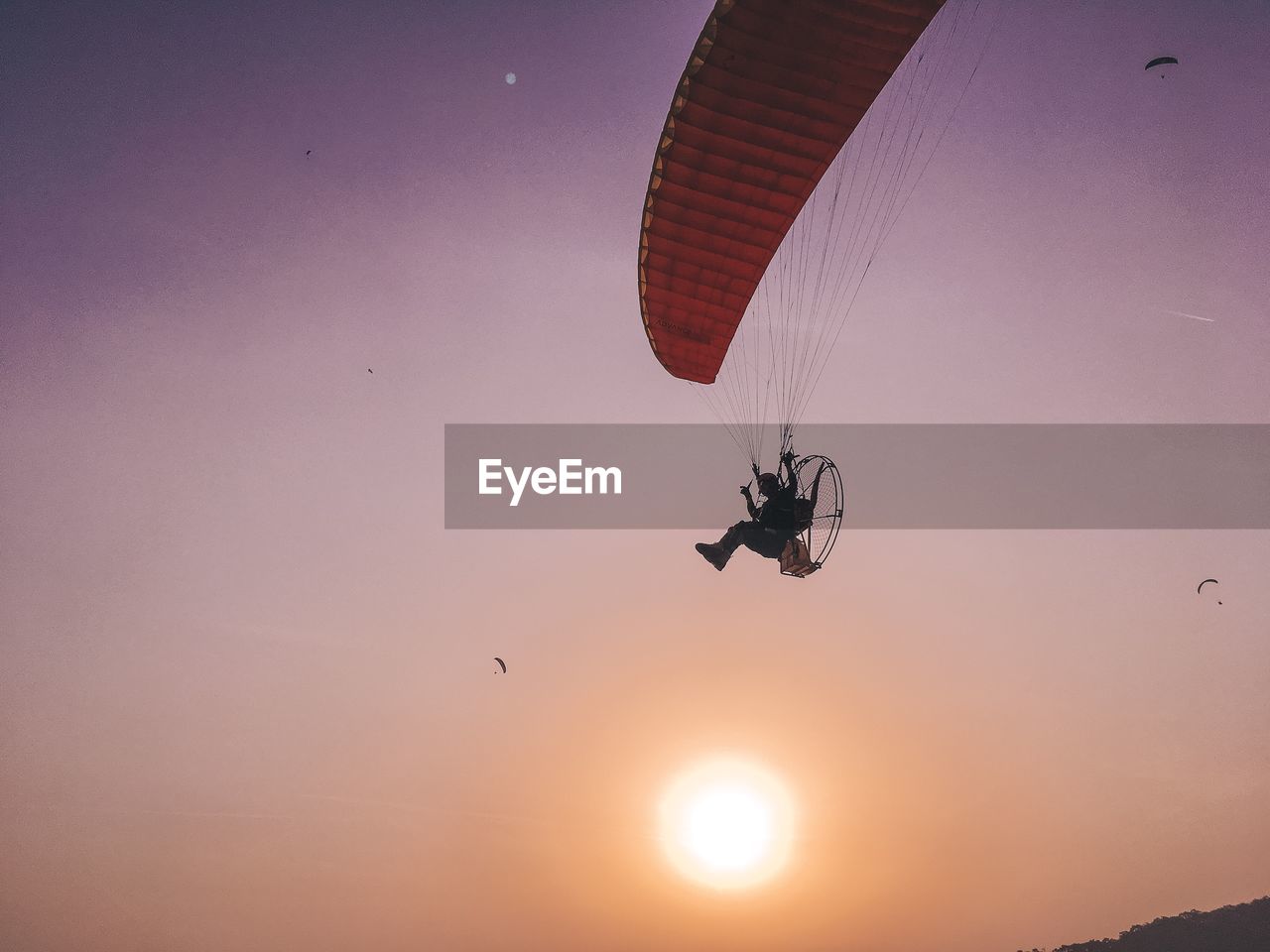 Low angle view of man powered paragliding during sunset