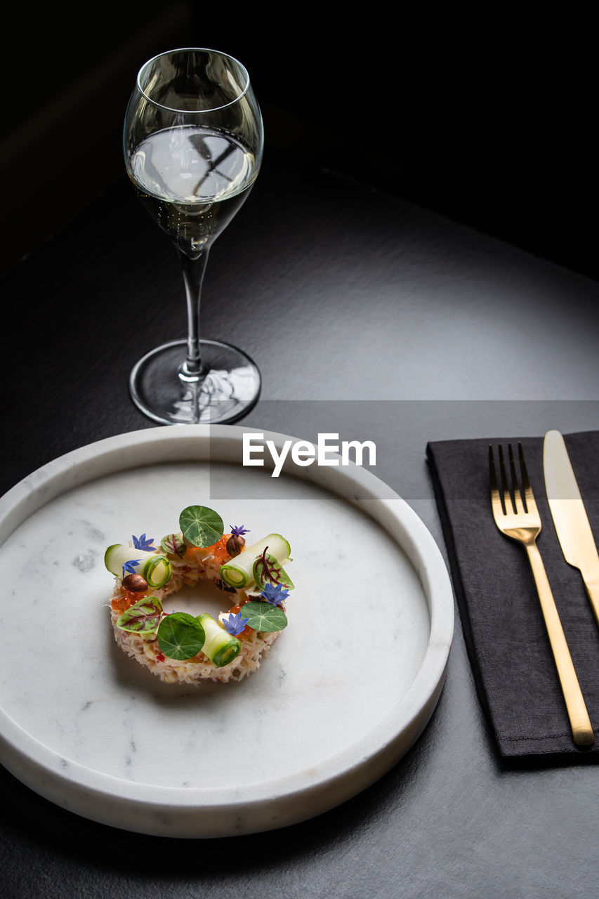 Appetizing snack with crab near decorated with cucumber rolls and caviar served on black background with cutlery in restaurant