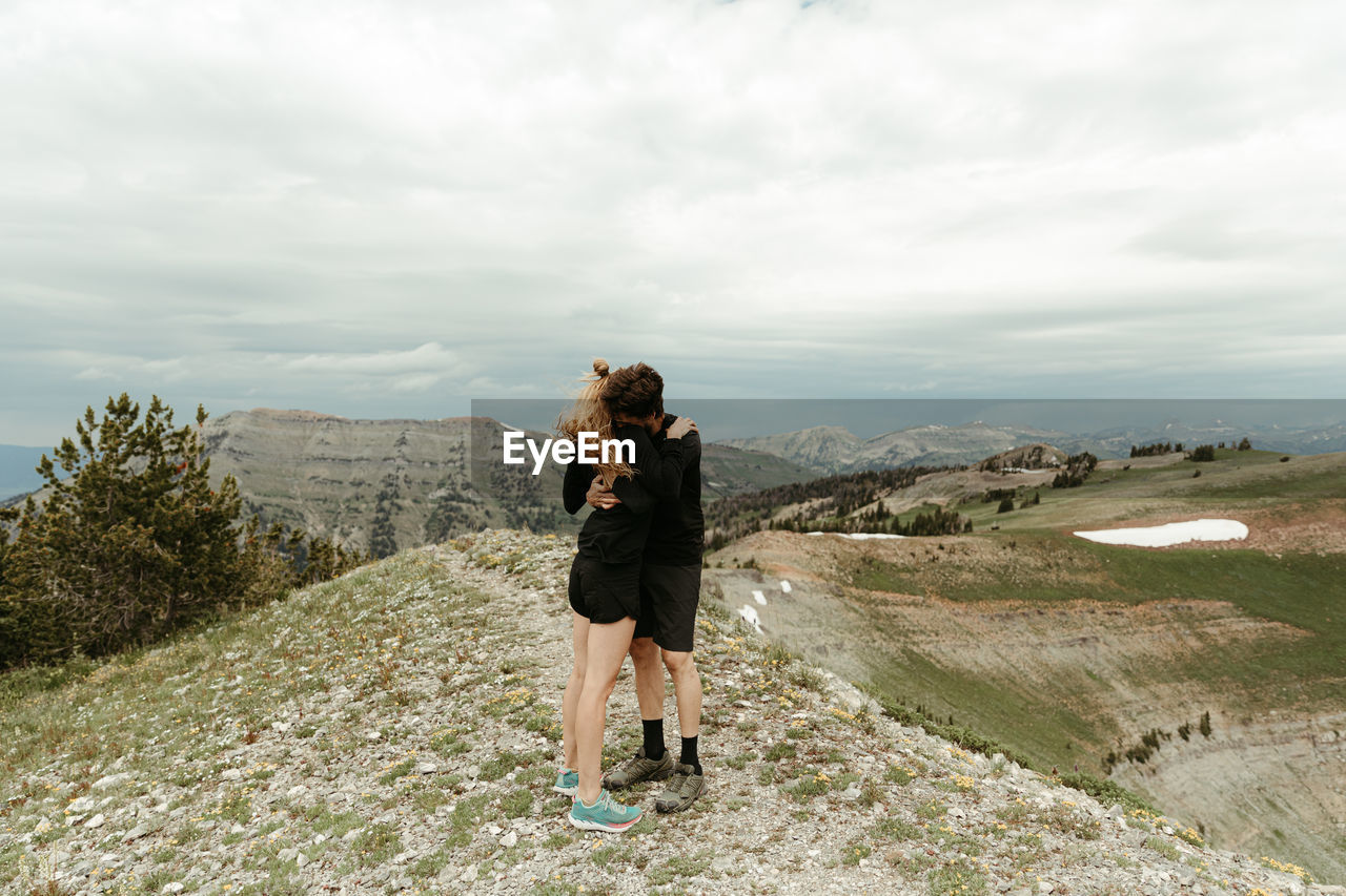 Engaged couple in all black embrace hug on windy ridge top in wyoming