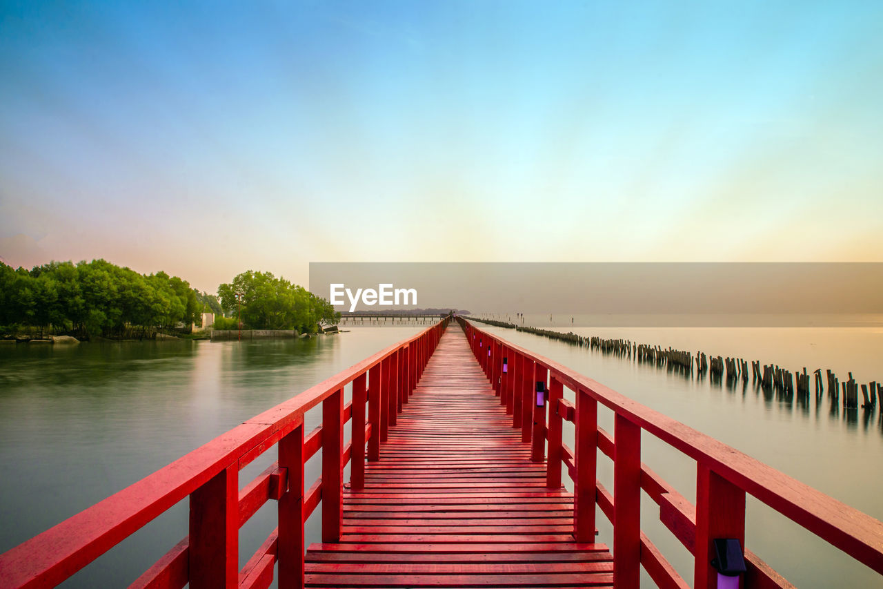 Wooden bridge over calm lake against sky