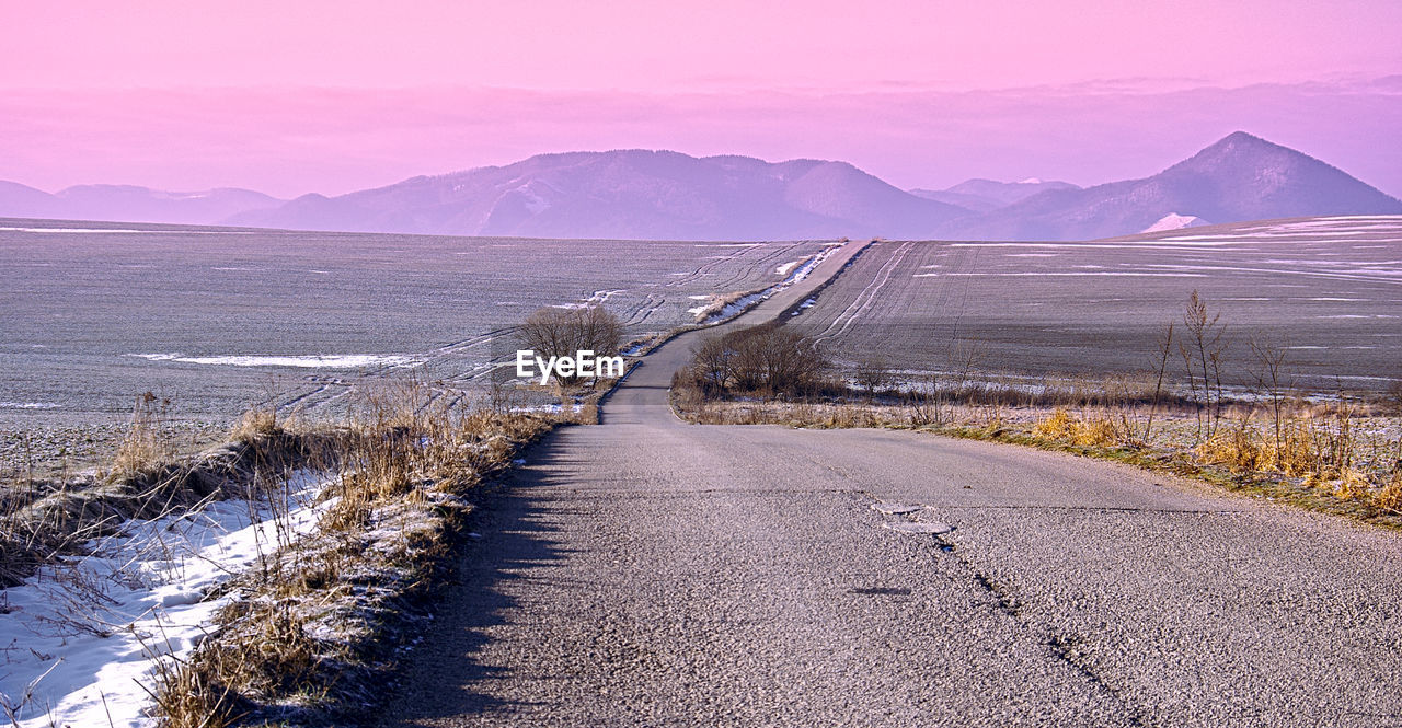 Road by mountains against sky during winter