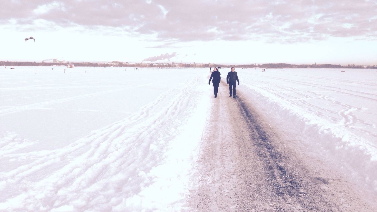 People walking on dirt road amidst snow covered landscape