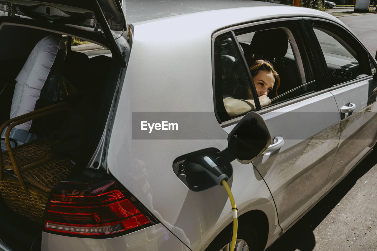 Electric car getting charged while girl looking through window at gas station on sunny day