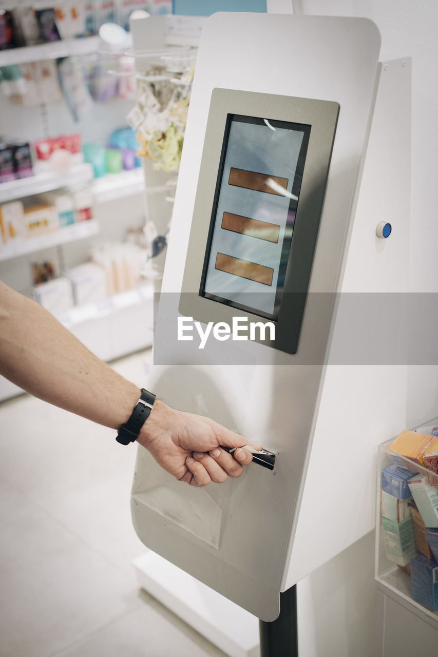 Cropped hand of male customer using kiosk at pharmacy store