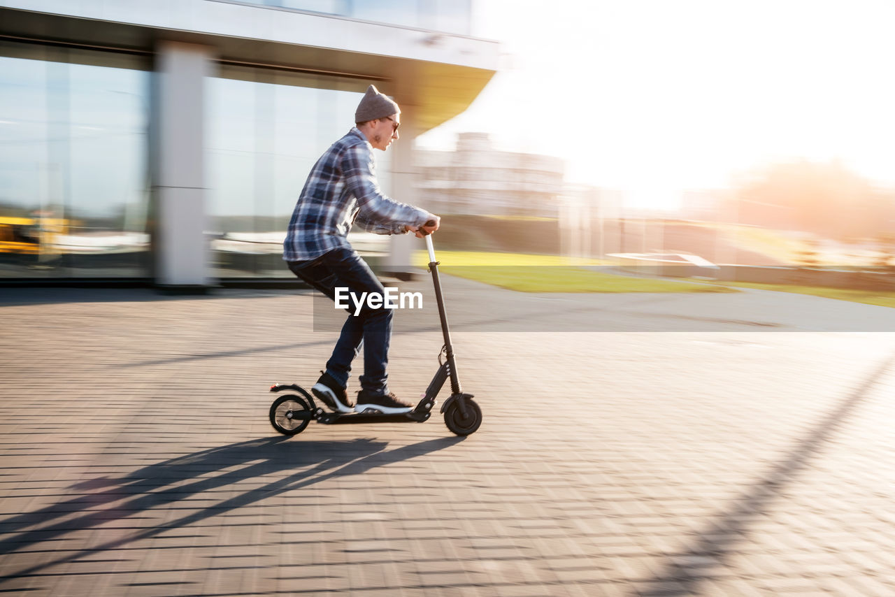 Side view of man riding push scooter on footpath