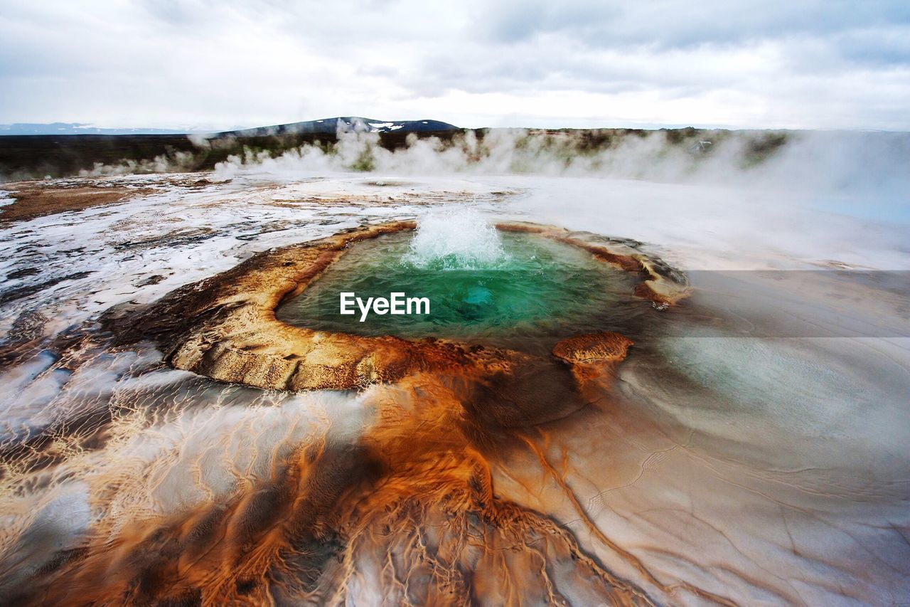 High angle view of geyser and field against cloudy sky