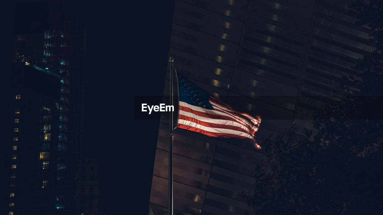 LOW ANGLE VIEW OF FLAG AGAINST BUILDINGS AT NIGHT